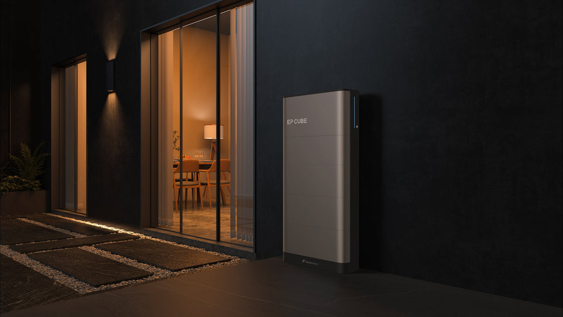 A grey inverter and battery stack of Canadian Solar EP Cube positioned outside at night with a patio door next to it leading to a softly lit living room